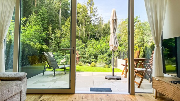 A modern living room with a sliding glass door leading to a patio with outdoor furniture and a TV. - modern, luxury, private entrance, garden, terrace, and stunning mountain views. (Brixen)