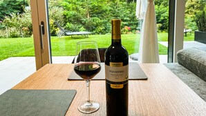 A bottle of Marzemino wine and a glass on a table with a view of a garden and outdoor seating area. - modern, luxury, private entrance, garden, terrace, and stunning mountain views. (Brixen)