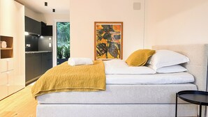 A modern bedroom with a bed, a painting, a view of greenery, and a kitchenette. - modern, luxury, private entrance, garden, terrace, and stunning mountain views. (Brixen)