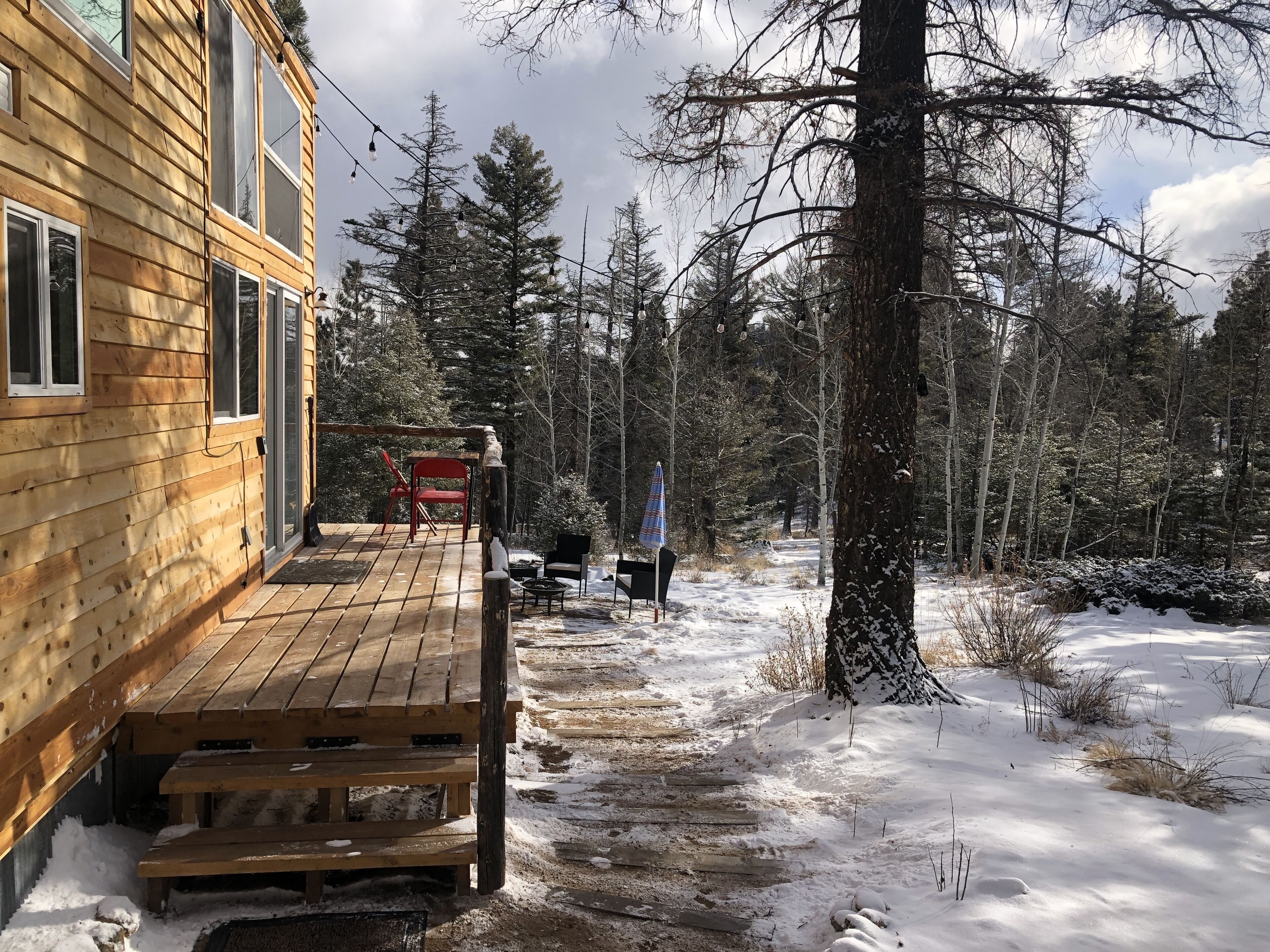 Una cabaña de madera con terraza, rodeada de nieve y árboles.