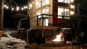 A wooden cabin with multiple windows and a fire pit in the foreground.