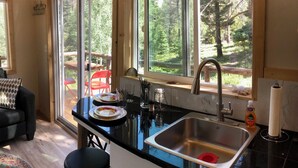 A kitchen with a large window, a sink, and a dining area with a red chair.
