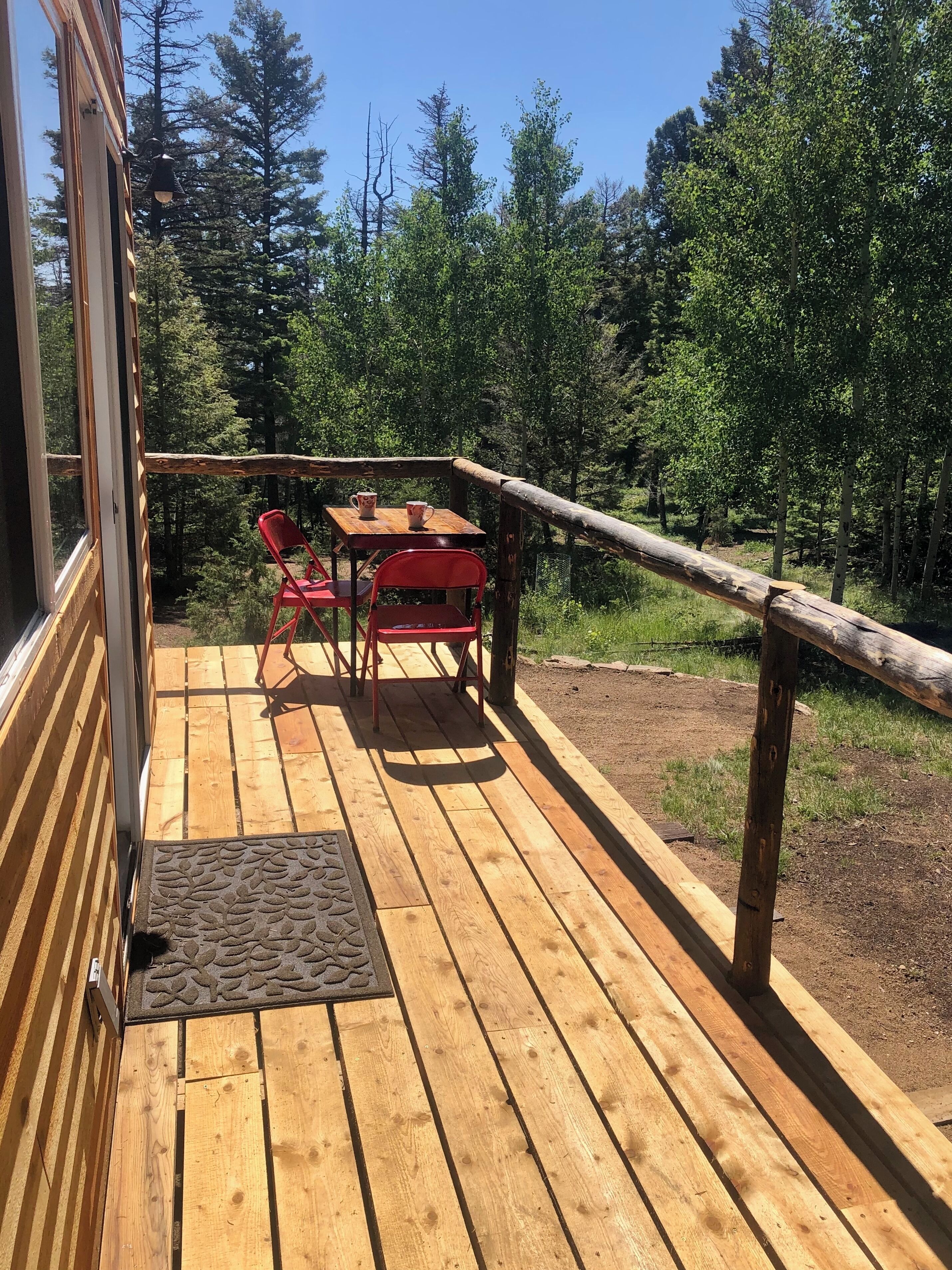 Una terraza de madera con una mesa y sillas, con vista a un área boscosa.