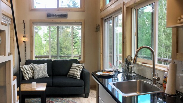 A modern kitchen with a black countertop, stainless steel sink, and large windows offering views of the outdoors.