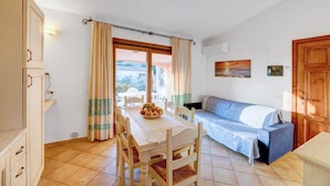 A room with a dining table, chairs, a sofa, a wooden cabinet, and a window with curtains. - The Fantastic Residenza Badus 1 Bedroom Apartment B4 Sleeps 4 (Badesi)