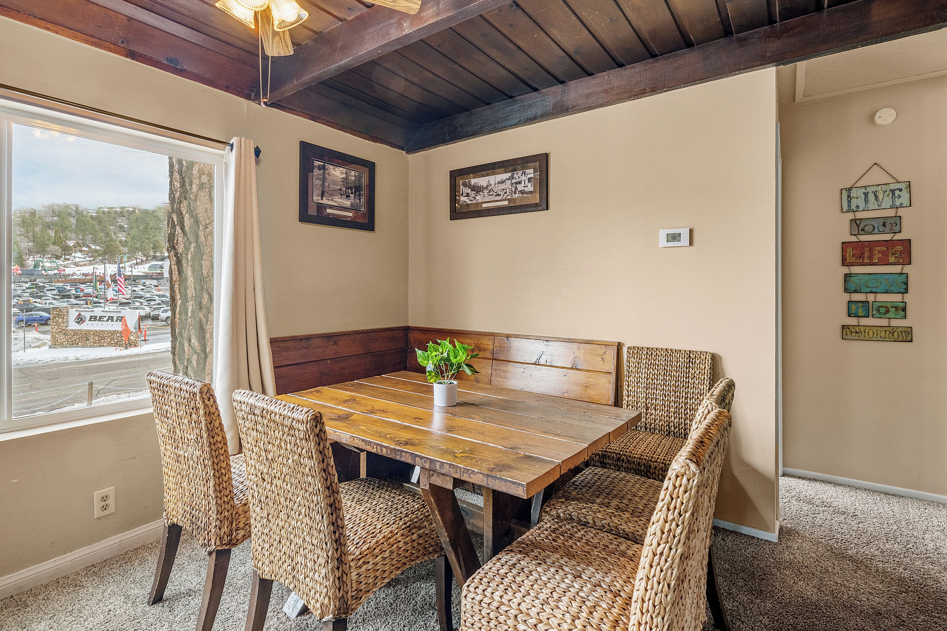 A dining area with a wooden table and woven chairs, a potted plant, and framed pictures on the wall.