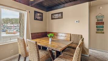 Un comedor con mesa de madera y sillas tejidas, una planta en maceta y cuadros en la pared.