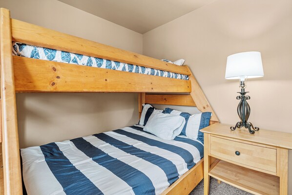 A bunk bed with a striped bedspread, a bedside table with a lamp, and a wooden nightstand.