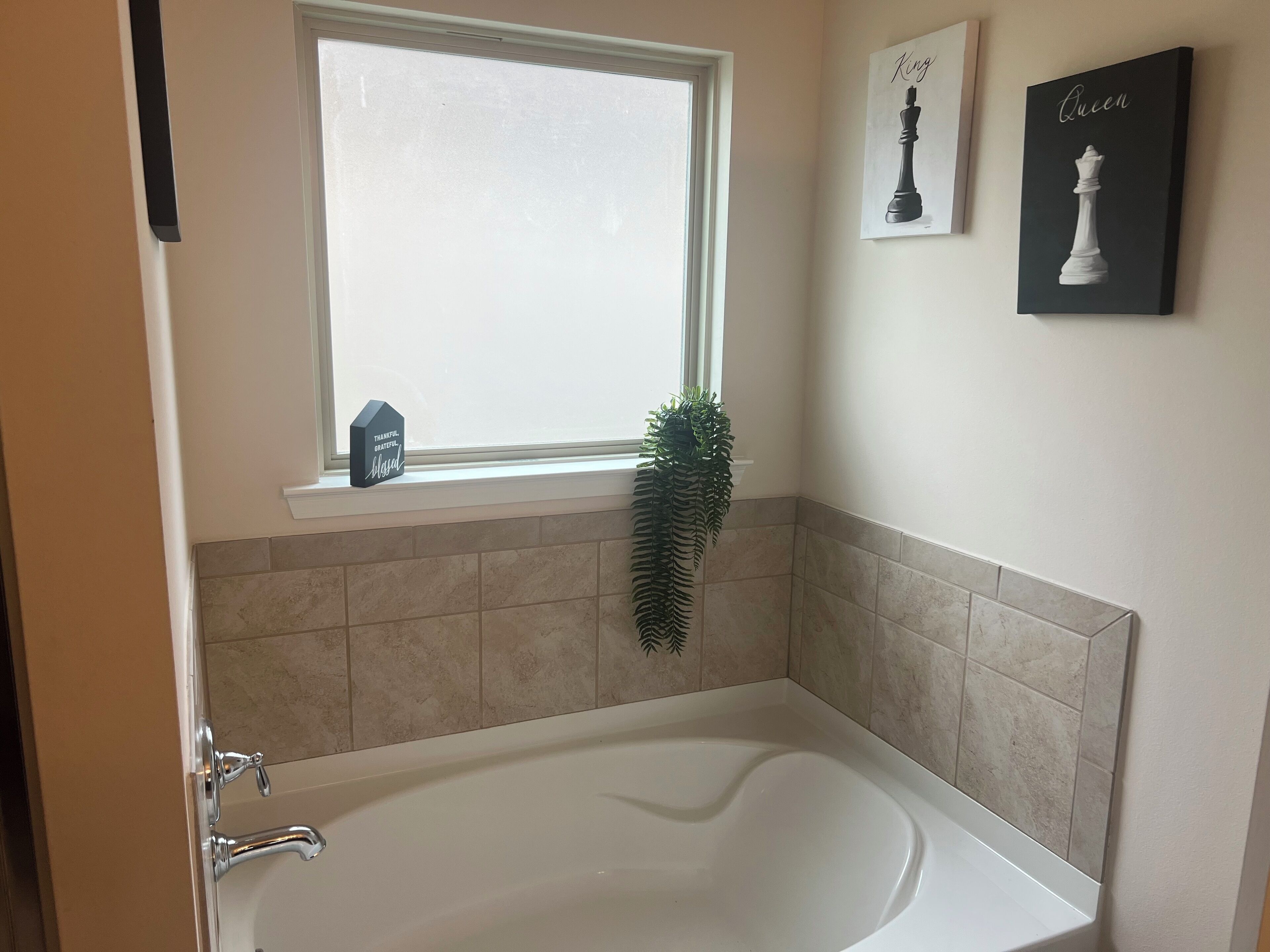 Une salle de bain avec une baignoire, une fenêtre, une plante en pot et des décorations murales sur le thème des échecs.