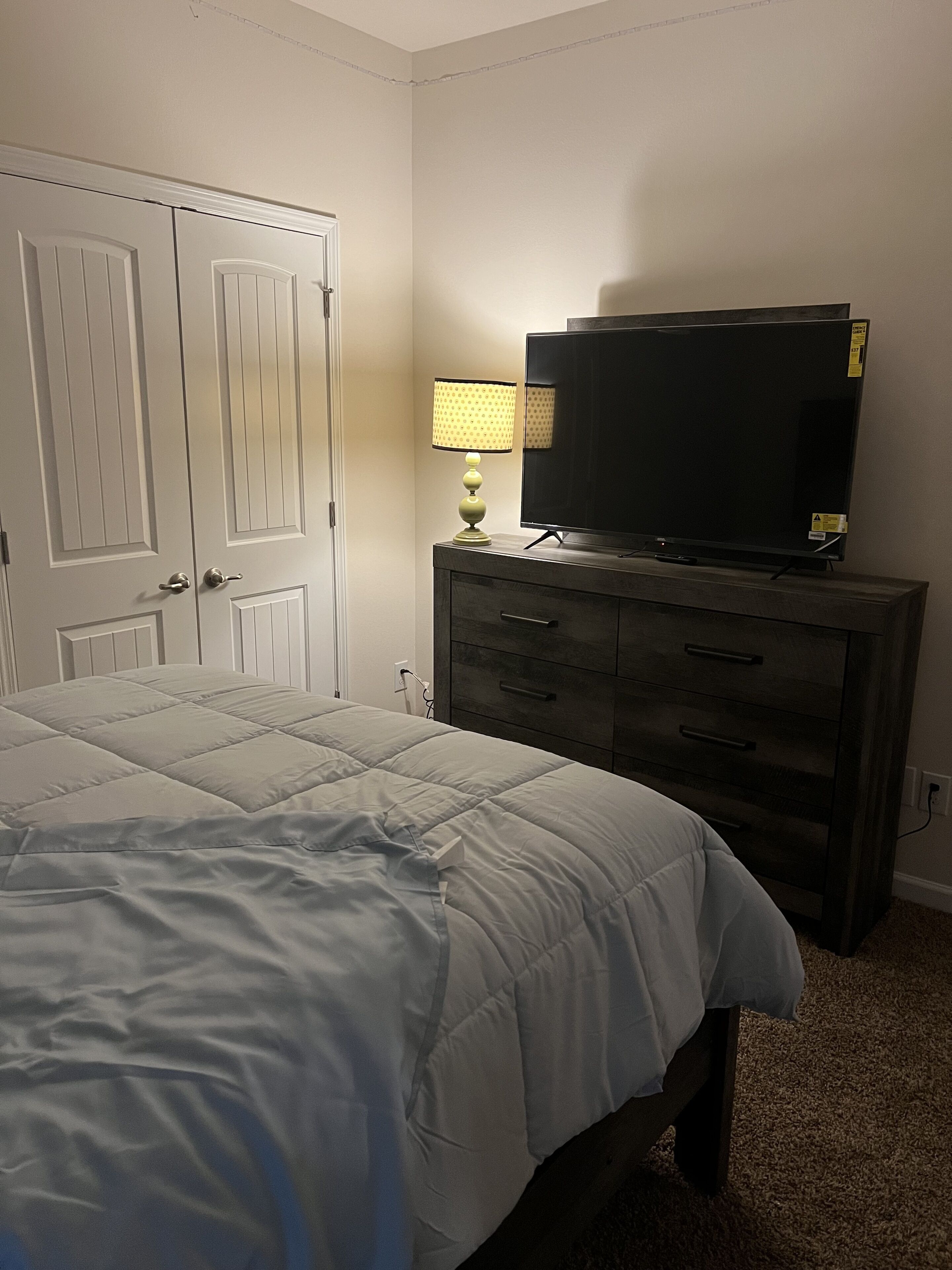 Une chambre à coucher avec un lit, une commode, un téléviseur et une lampe.