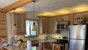 A modern kitchen with wooden cabinetry, stainless steel appliances, a large island with bar stools, and a hanging pendant light. - Cozy two bedroom cabin with hearty Firewood Stove/Game Room (Springville)
