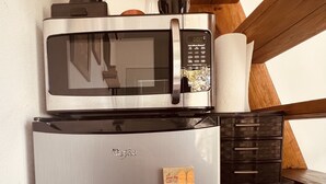 Une cuisine compacte équipée d’un réfrigérateur en acier inoxydable, d’un four à micro-ondes et d’une machine à café placés sur le plan de travail.