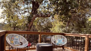 Une terrasse en bois avec deux fauteuils en osier et une table ronde, le tout entouré d’arbres.