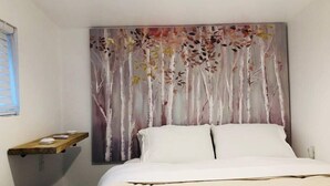 Une chambre à coucher avec un lit, une table de chevet et un tableau représentant des arbres, accroché au mur.