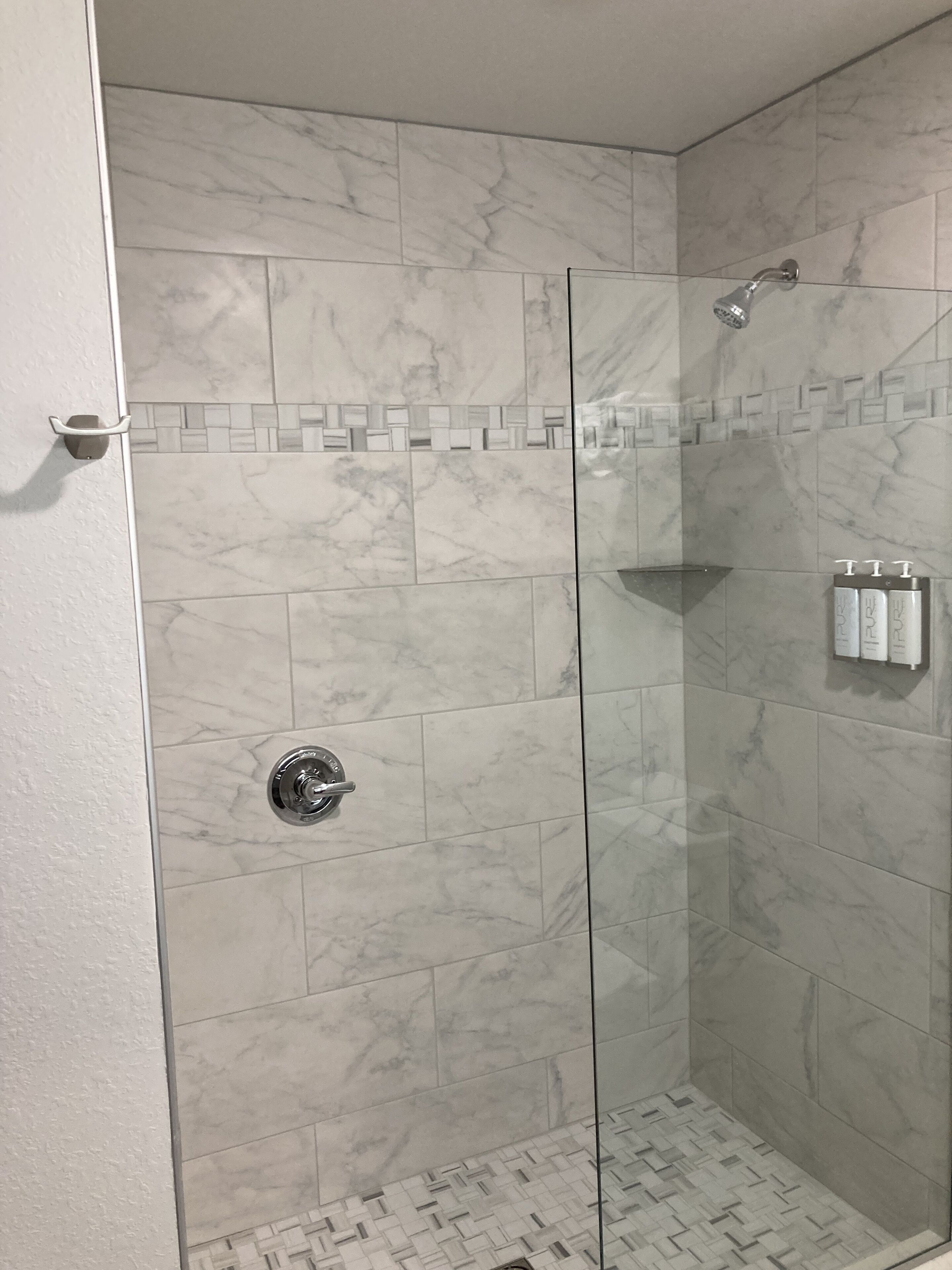 Una ducha con paredes de vidrio, azulejos de mármol y piso de cerámica.
