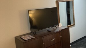 Camera d'albergo con un comò in legno, una TV a schermo piatto, uno specchio e un piccolo cartello sul comò.