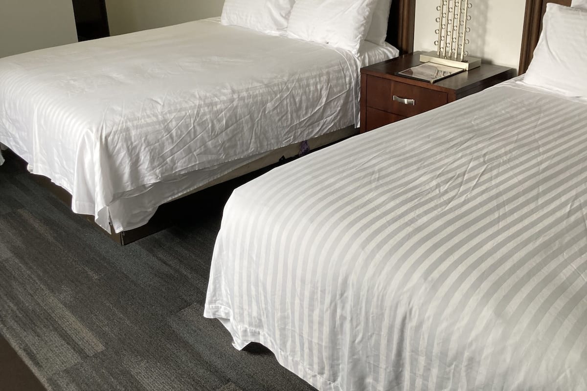 Duas camas de solteiro com roupa de cama branca, cabeceiras de madeira e mesas de cabeceira com luminárias.