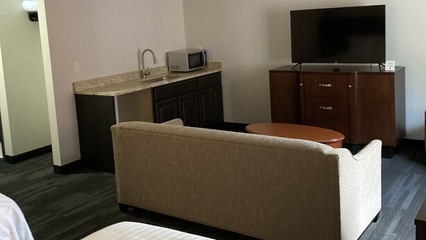 Una camera d'albergo con un letto, un divano, una televisione, un forno a microonde e un angolo cottura.