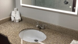 Un bagno con un piano in granito, un lavandino bianco, un grande specchio con illuminazione integrata e un box doccia in vetro.