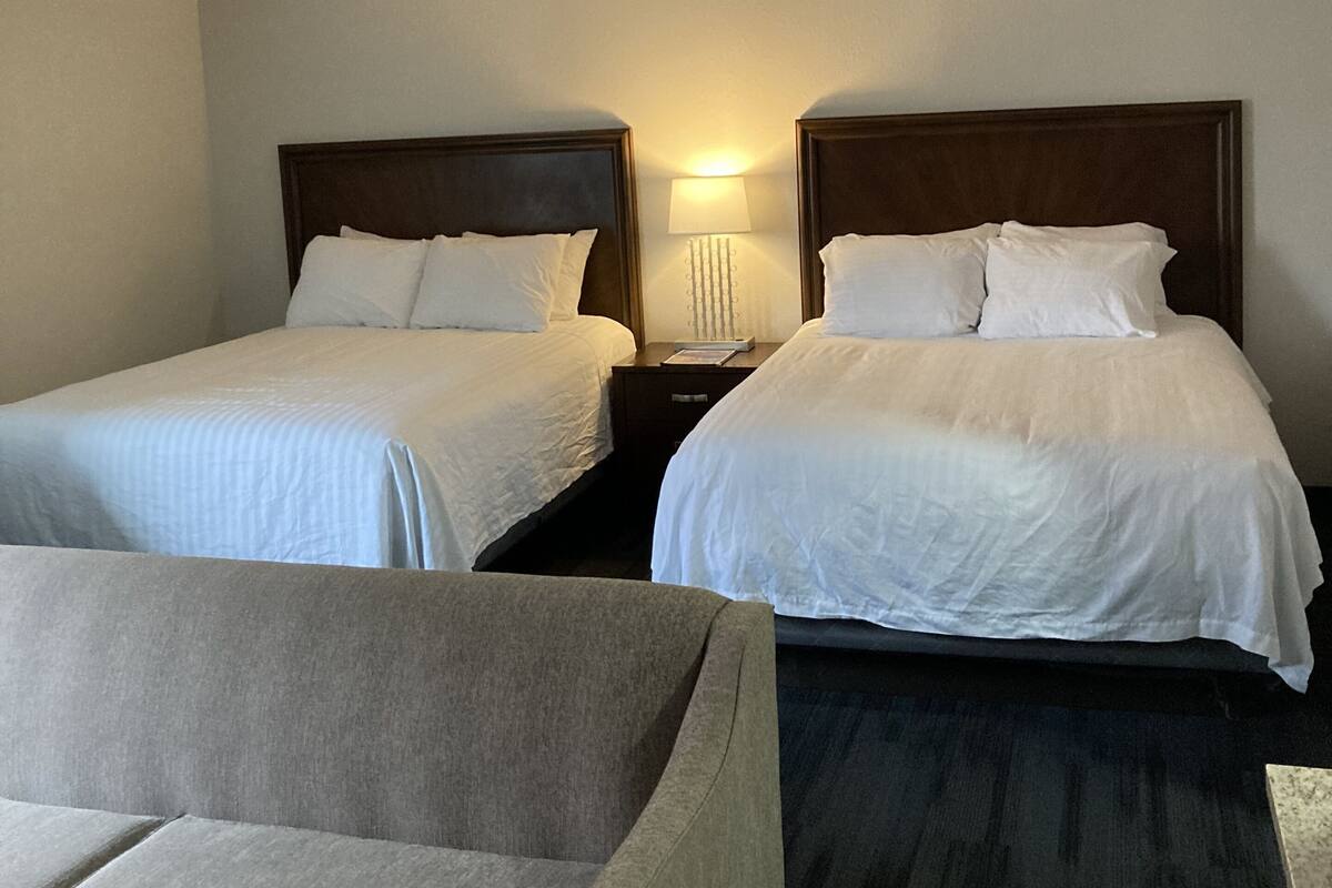 Quarto de hotel com duas camas de solteiro, uma mesinha de cabeceira com abajur e um sofá.