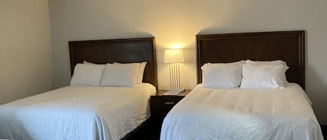 A hotel room with two single beds, a bedside table with a lamp, and a sofa.