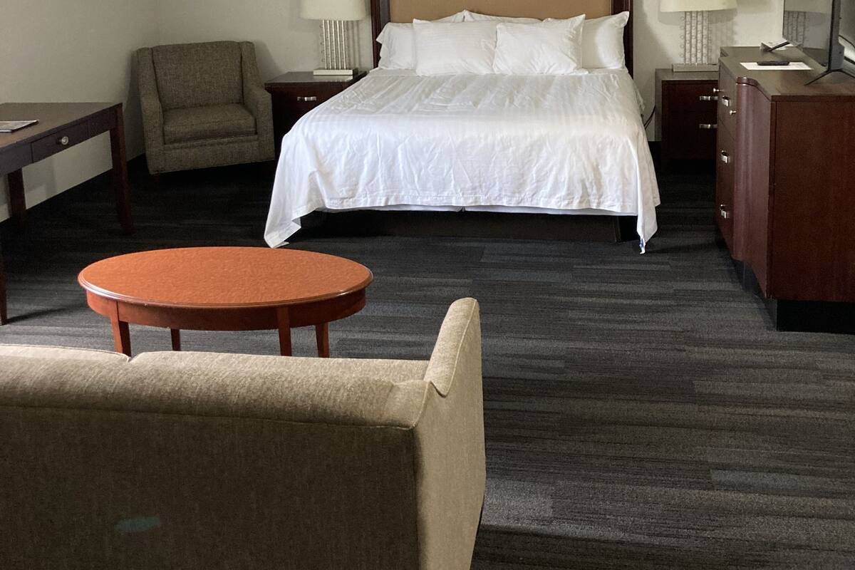 Quarto de hotel com cama, cadeira, escrivaninha, mesa, cômoda e espelho.