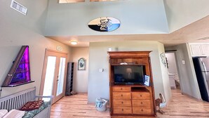 Un espace de vie à plusieurs niveaux comprenant un meuble de rangement en bois servant d’espace de divertissement, un ventilateur de plafond et une vue sur l’étage supérieur par une fenêtre.