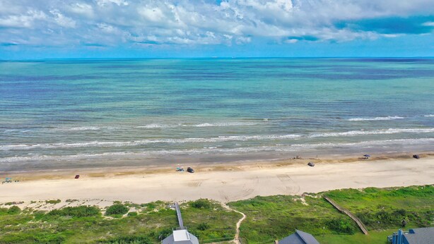 Une plage avec une eau turquoise et limpide, un rivage sablonneux et une zone herbeuse dotée d’une promenade en bois.