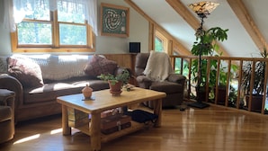 Uma sala de estar aconchegante com piso de madeira, um sofá, uma poltrona, uma mesa de centro e uma planta em vaso.