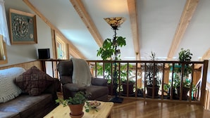 Uma sala de estar aconchegante com teto de madeira, um sofá confortável, mesa de centro de madeira e diversos vasos com plantas.
