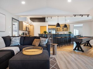A modern living room with a sofa, a pool table, and a kitchen in the background.