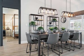 A modern dining area with a dark wooden table, grey chairs, and pendant lighting.