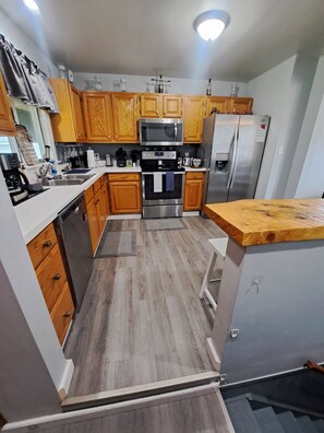 A modern kitchen with wooden cabinets, stainless steel appliances, and a wooden countertop.