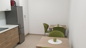 Eine kleine Küche mit Kühlschrank, Spüle und einem Esstisch mit Stühlen.