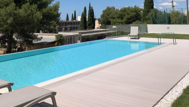 Ein Swimmingpool mit Holzterrasse, Liegestuhl und einem Baum im Hintergrund.