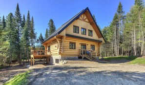 A log cabin with a balcony, surrounded by a forest.