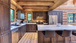 Een moderne keuken in een blokhutstijl met houten balken, roestvrijstalen apparatuur en een groot kookeiland met barkrukken.