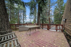 A wooden deck with a table and benches, surrounded by tall trees and a view of a cabin. - Comfy Cubby  (Big Bear Lake)