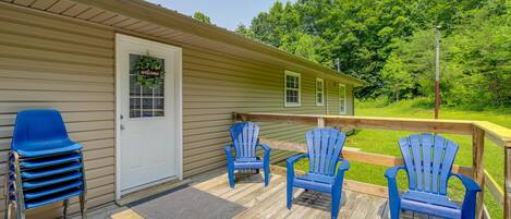 A wooden deck with blue Adirondack chairs, a door with a 'Welcome' sign, and a view of a green landscape.