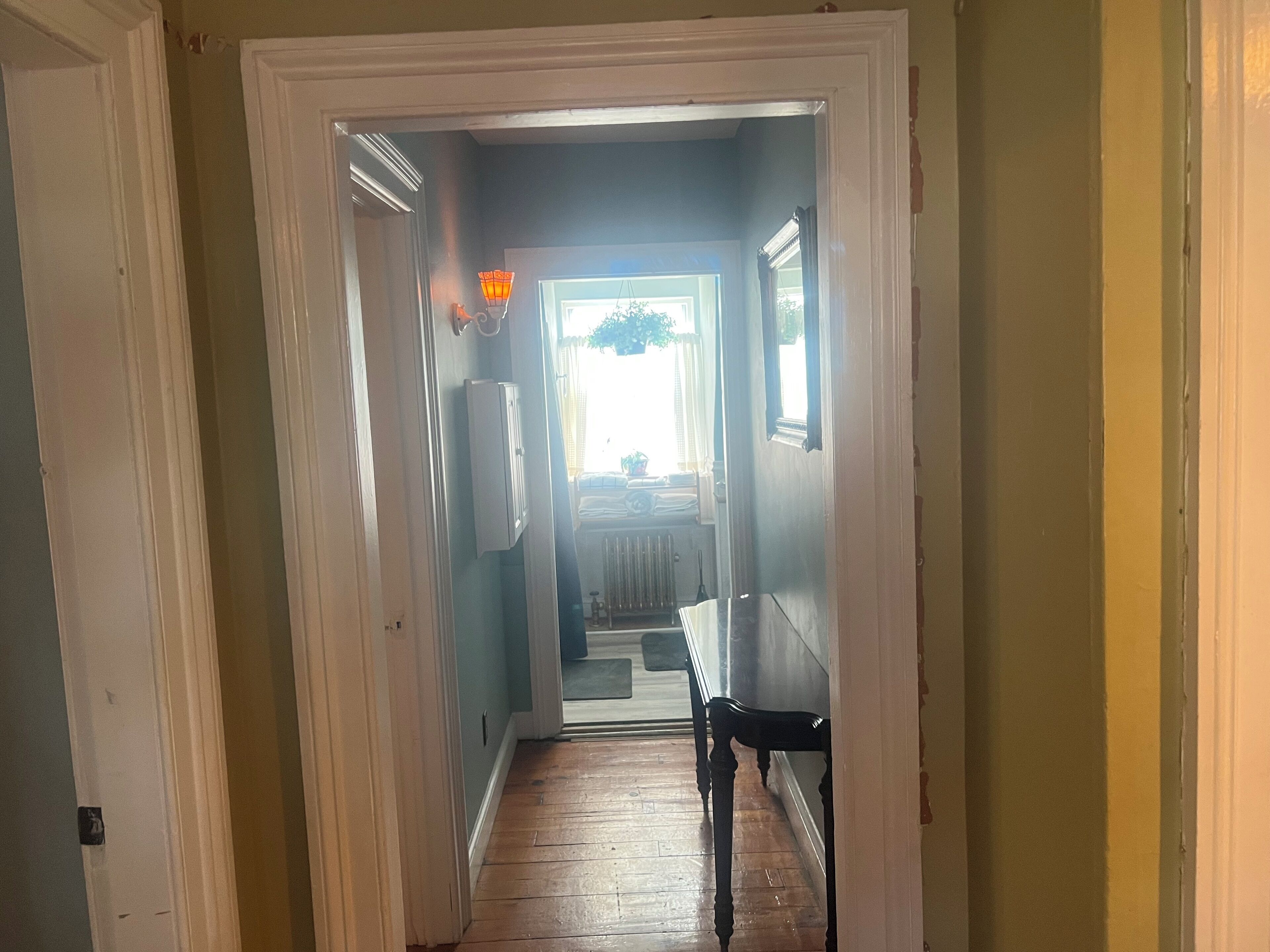 A narrow hallway with wooden flooring, a bench, and a radiator.