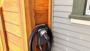 A wooden structure with a black charging cable connected to a charging station. - Urban Greenhouse (San Diego)