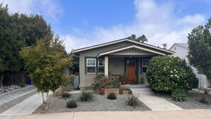 A single-story house with a front porch, a small garden with various plants, and a clear sky. - Urban Greenhouse (San Diego)