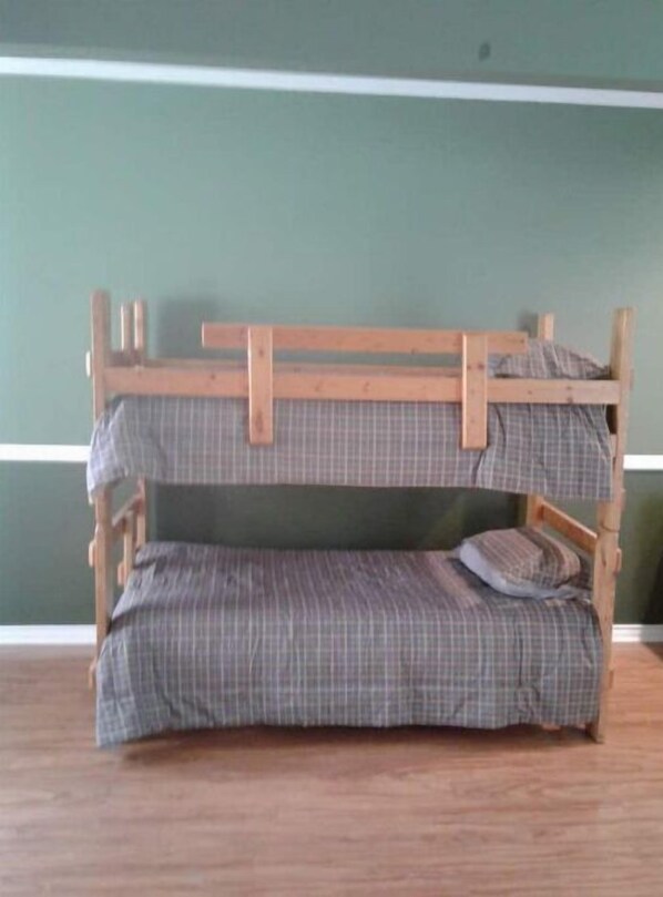 A bunk bed with a checkered mattress and wooden frame, set against a green wall.