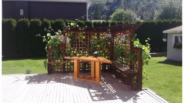 En træterrasse med et træbord og bænke, omgivet af et espalier med slyngplanter.