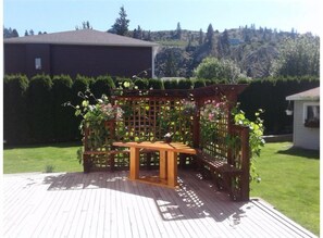 A wooden deck with a wooden table and benches, surrounded by a wooden trellis with climbing plants.