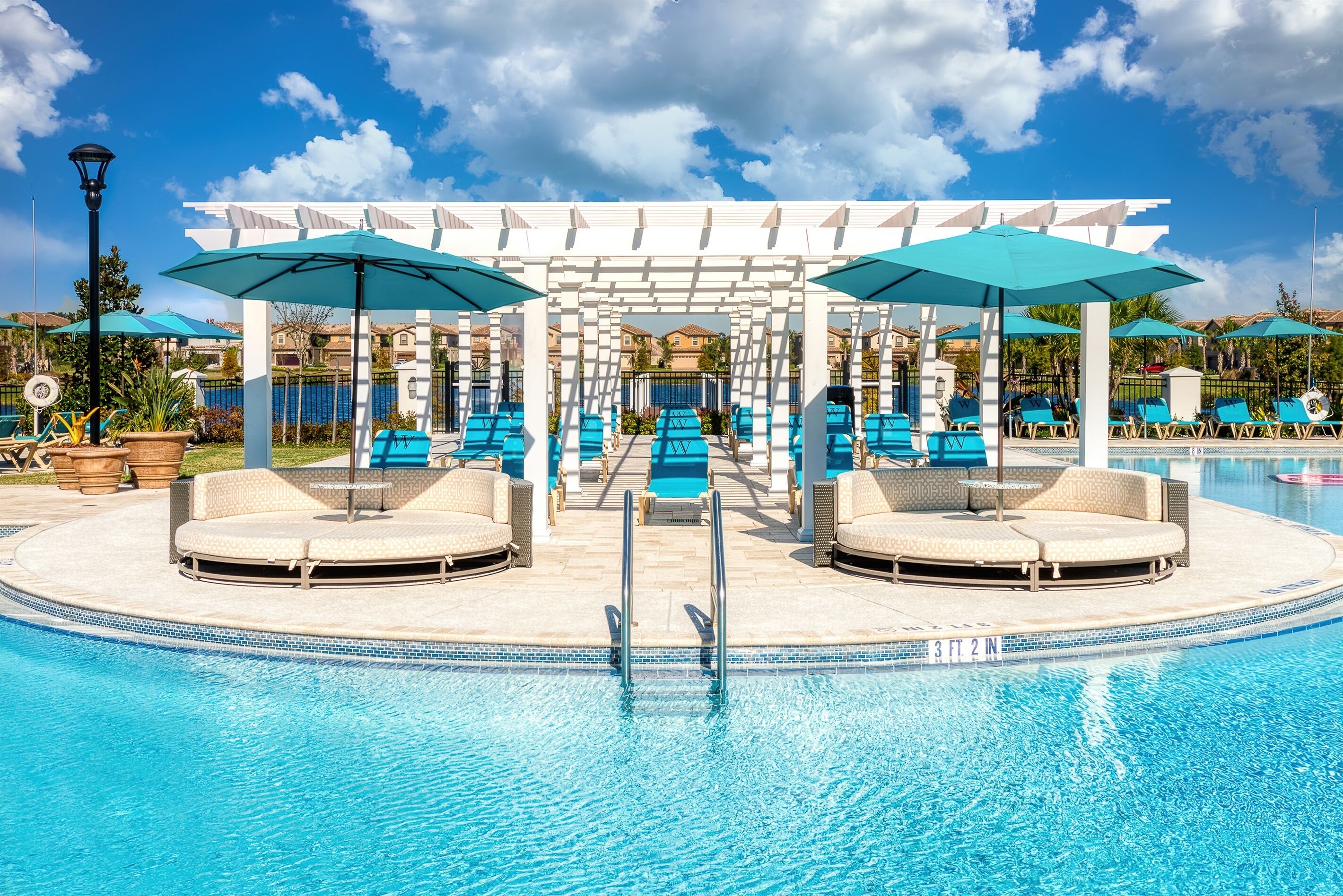 A pool area with lounge chairs and umbrellas, a pergola structure, and a clear blue sky.