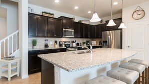 Una cocina moderna con gabinetes oscuros, electrodomésticos de acero inoxidable, encimera de granito e iluminación colgante.
