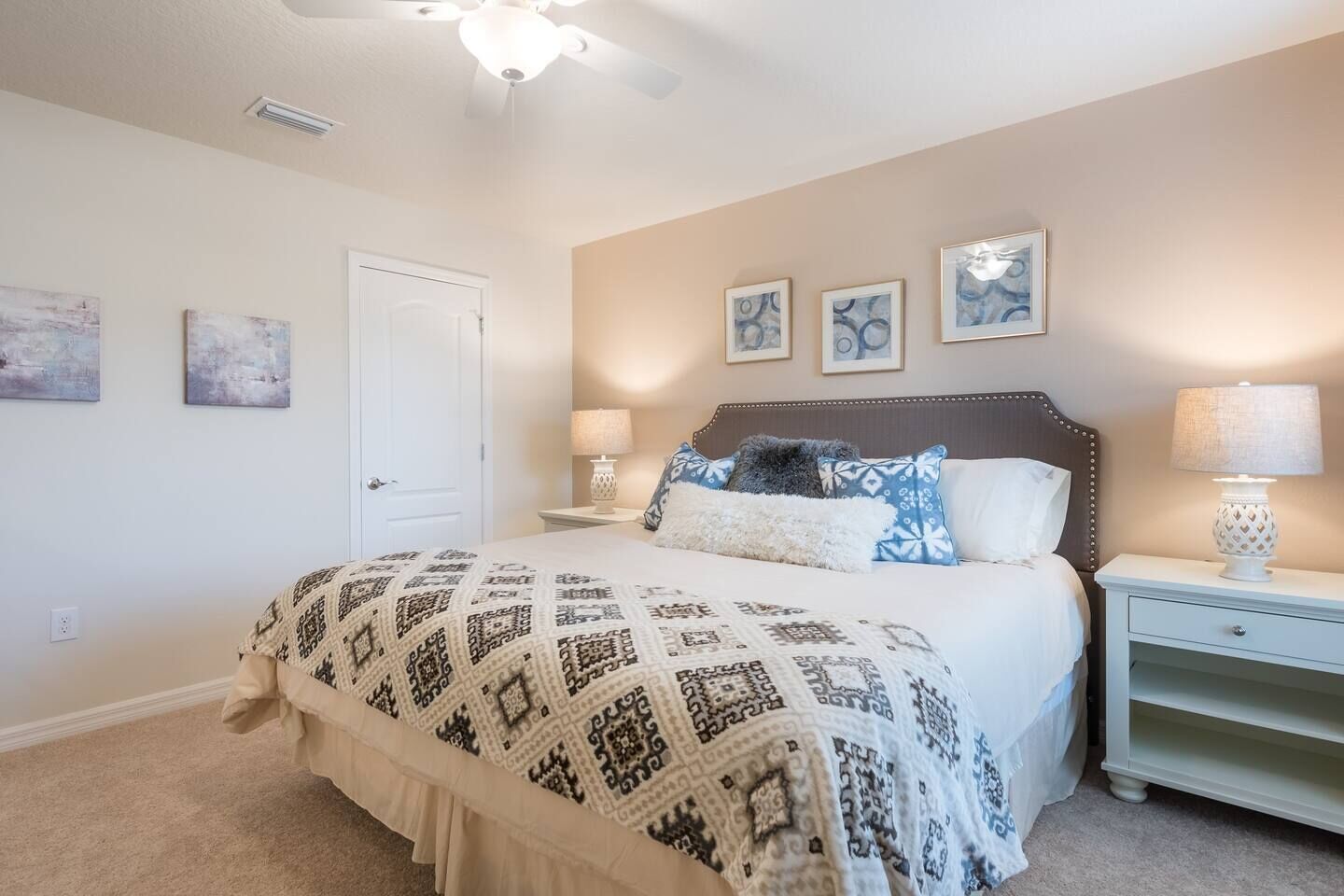 A bedroom with a bed, bedside tables, a ceiling fan, and wall art.