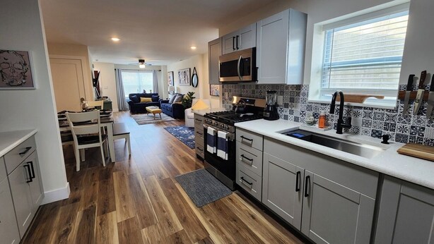 A modern kitchen with grey cabinets, a black stove, and a tiled backsplash. - Fairview Terrace-Brand New 3BDRM, Central Location  (Atlantic City)