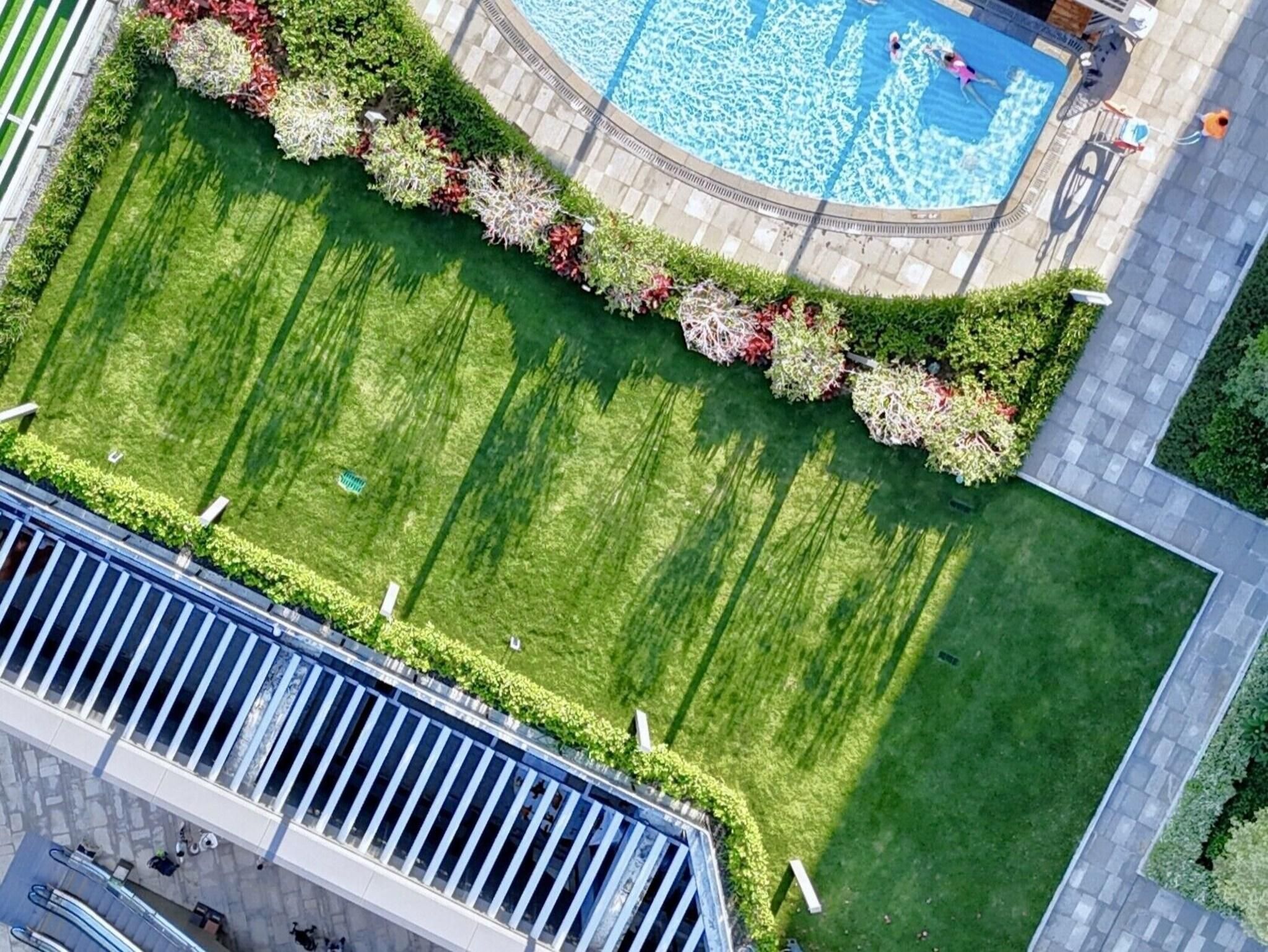 An aerial view of a landscaped area with a swimming pool, a well-manicured lawn, and a paved walkway.